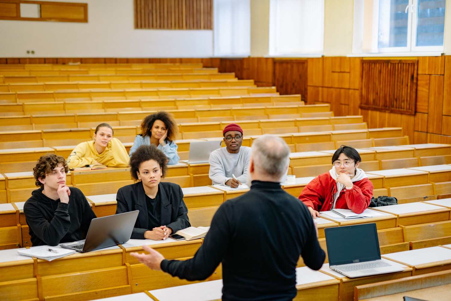 A professor lecturing a group of students in a large university hall with many open seats
