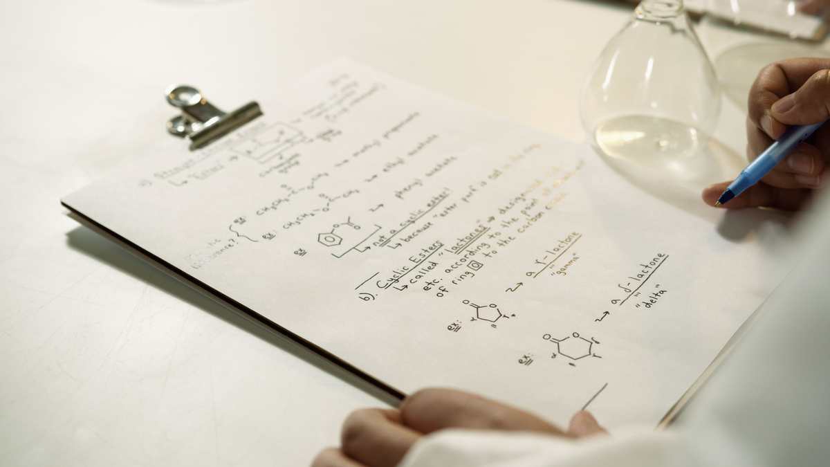Handwritten chemistry notes on a clipboard beside laboratory glassware