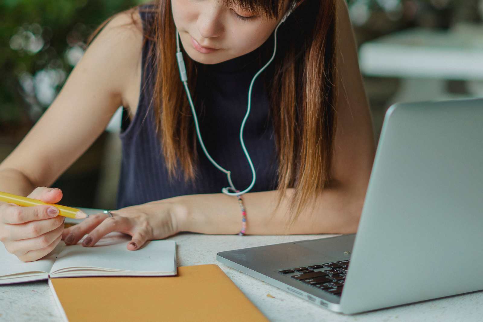 A student takes notes beside an open laptop while studying at a table