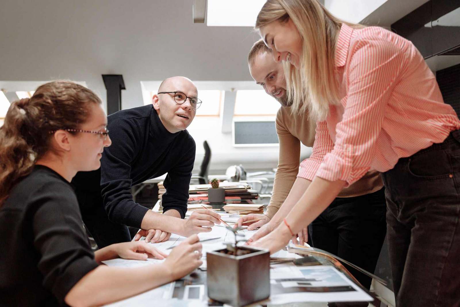 Four colleagues lean over a table covered in printed plans and sketches, collaborating closely