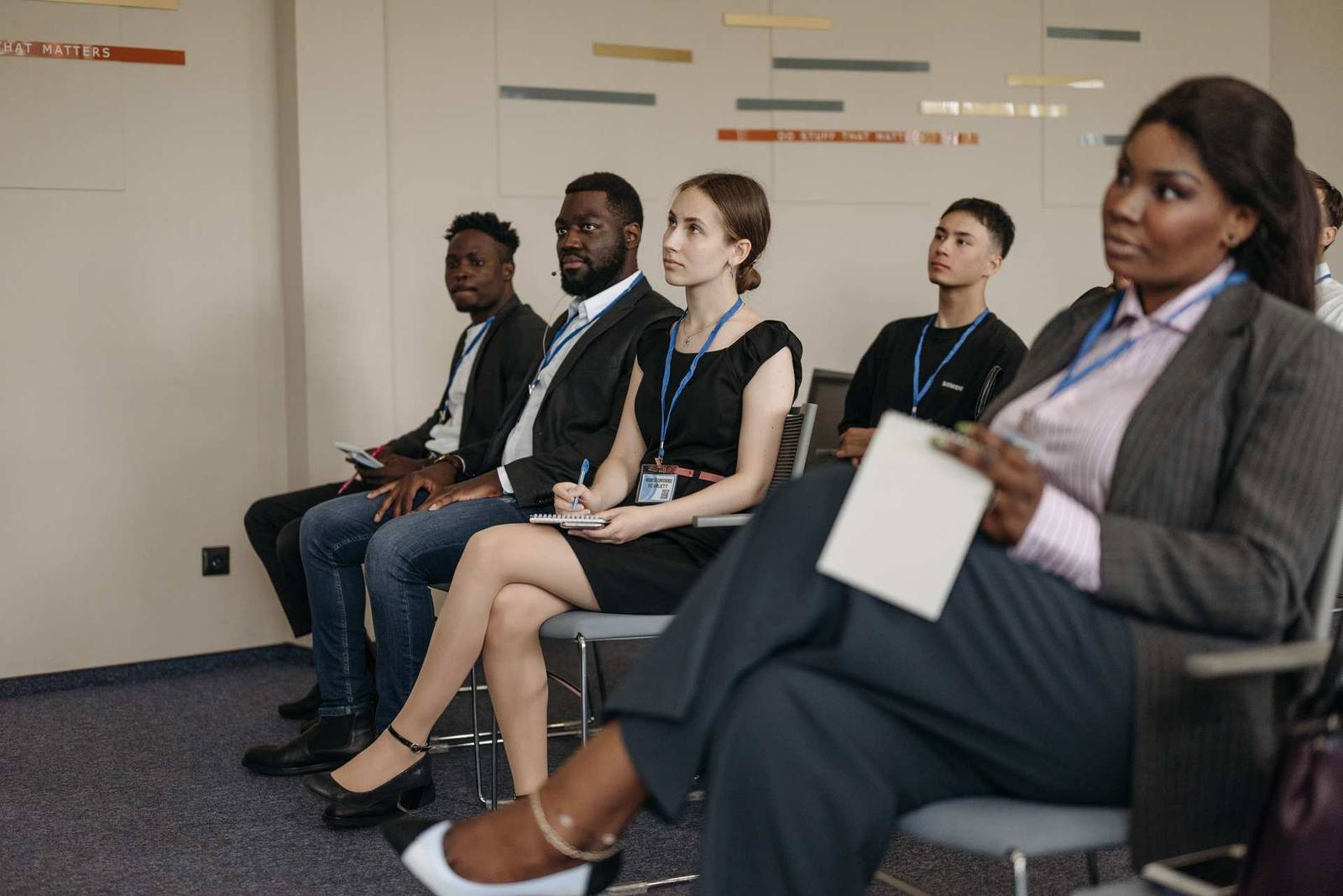 A row of professionals wearing lanyards sit and listen attentively during a meeting