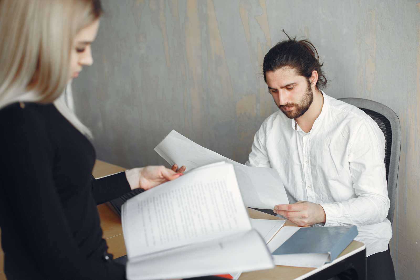 Two professionals page through printed documents across a desk