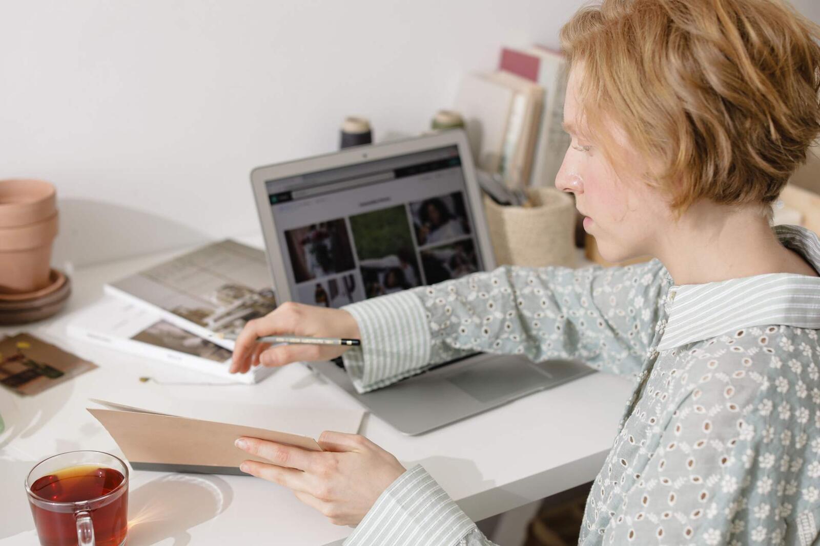 A woman at a desk points a pen toward a laptop screen while holding a folder