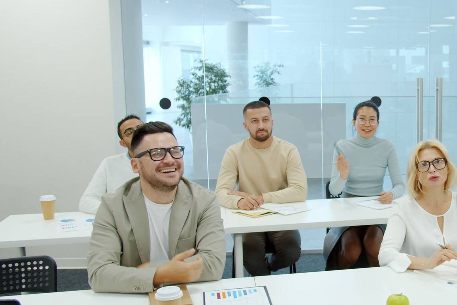 A man laughs while seated with colleagues at tables during a meeting