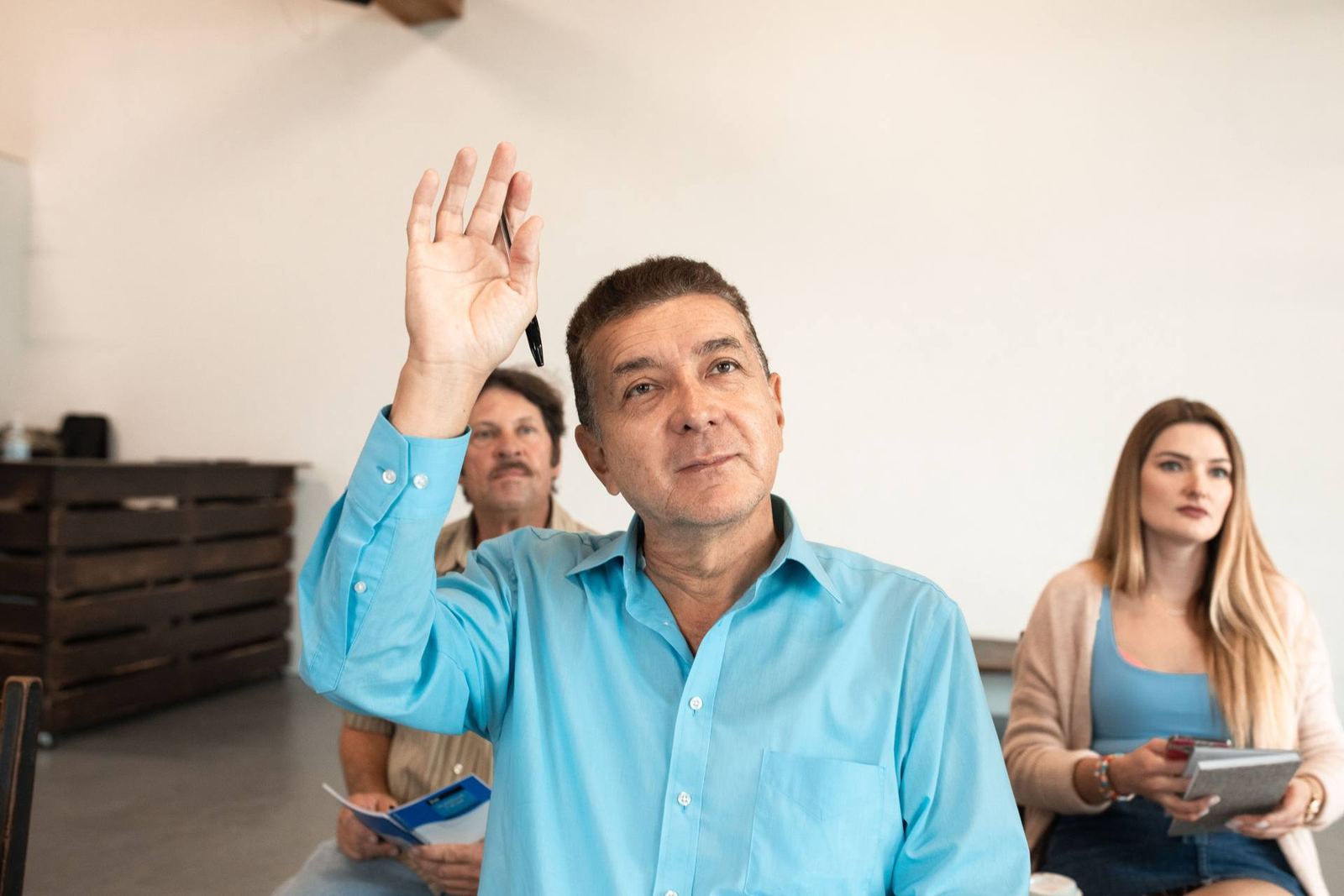 A man raises his hand to ask a question during a seminar, colleagues seated nearby