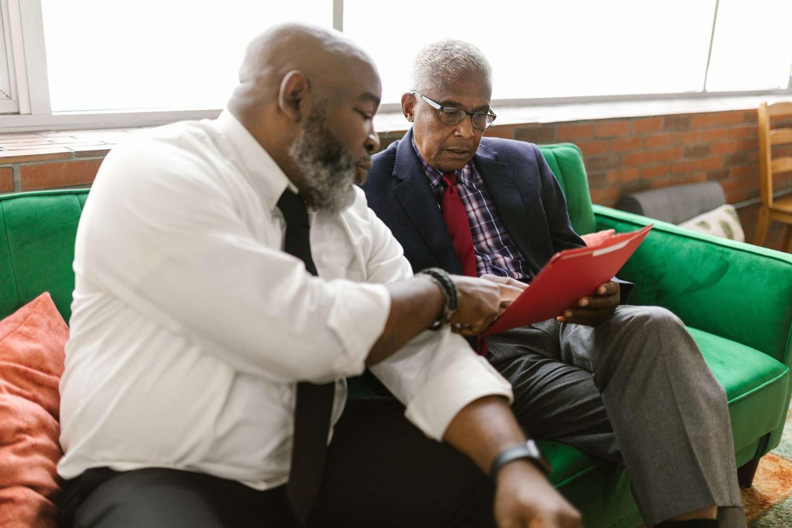 Two colleagues sit together reviewing a red folder, one pointing to a page while the other looks on
