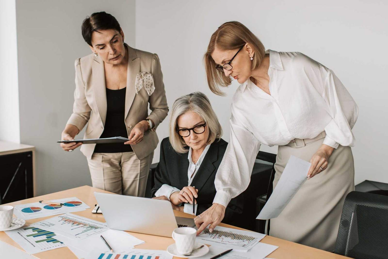 Three colleagues review printed charts and an open laptop together at a conference table