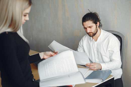 Two professionals page through printed documents across a desk