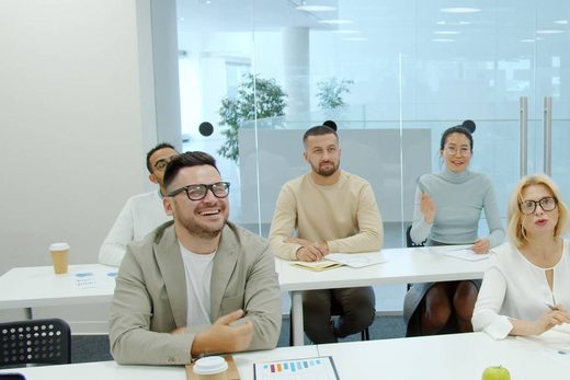 A man laughs while seated with colleagues at tables during a meeting