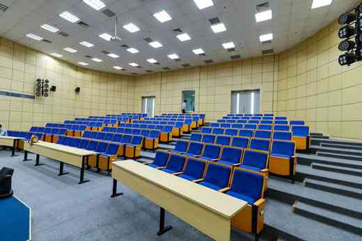 Rows of empty tiered seats in a lecture hall, lit by overhead panel lighting