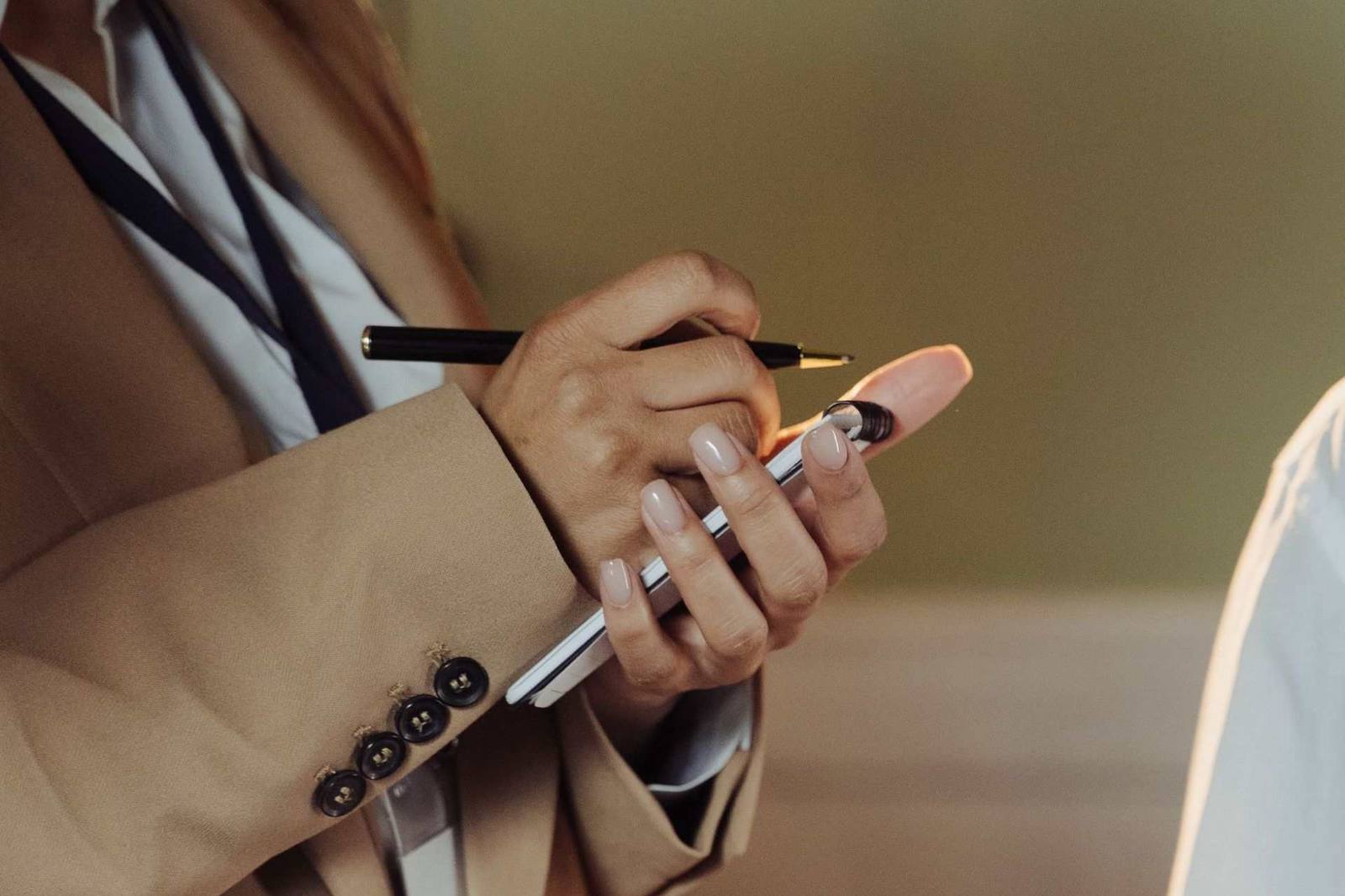 A close-up of a hand annotating a letter with a pen, an ID badge on a lanyard visible at the wrist
