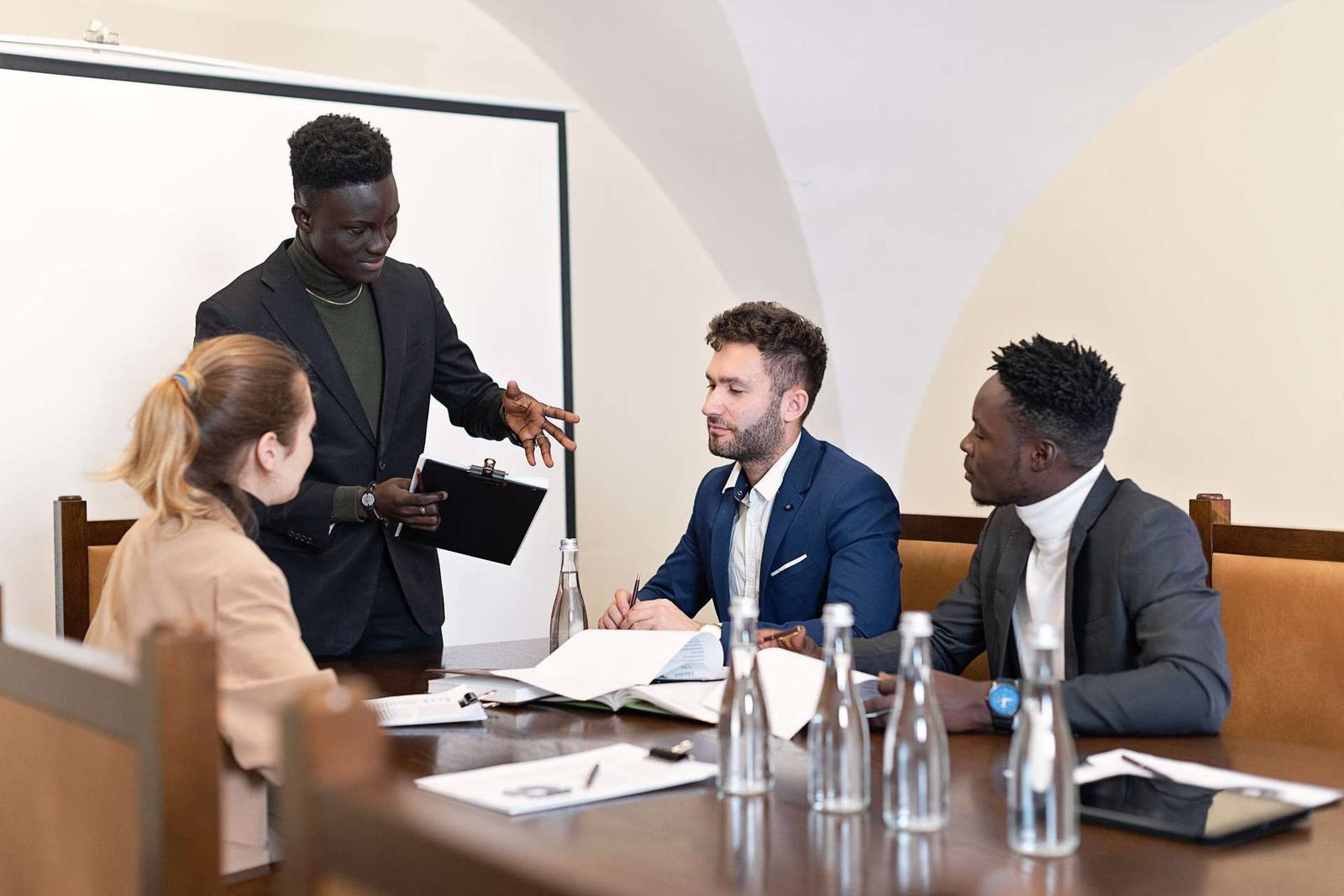 A colleague gestures while presenting to three seated colleagues around a conference table in a vaulted meeting room
