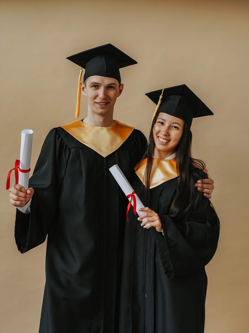 A man and a woman in graduation caps and gowns smiling and holding diplomas