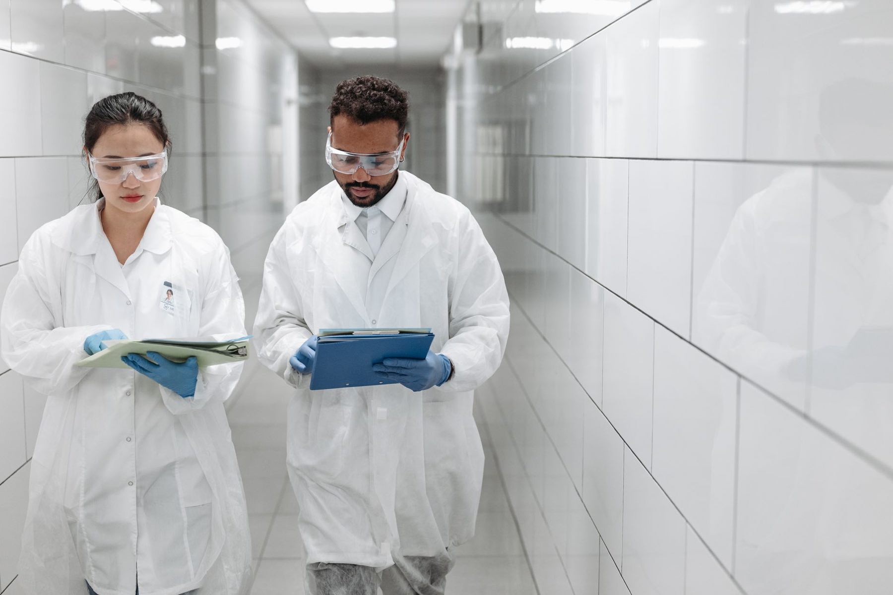 Two researchers in lab coats reviewing documents in a bright clinical corridor