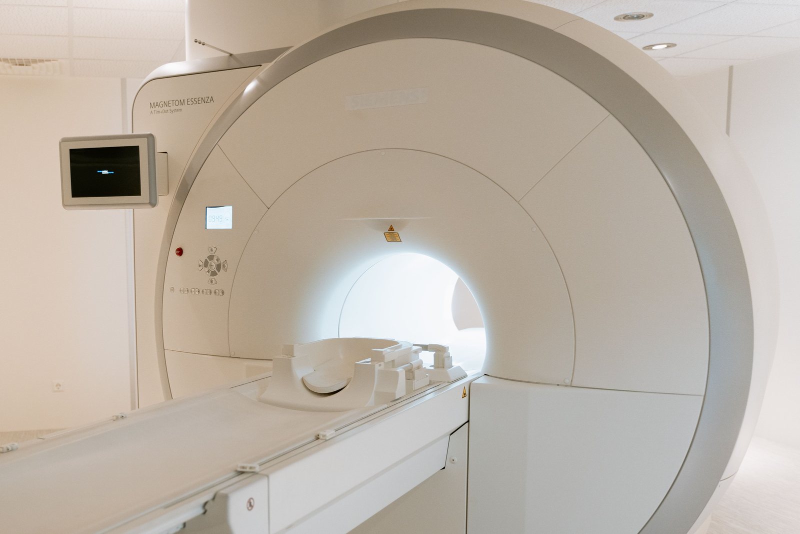An MRI scanner with its bore illuminated and the patient table extended, in a bright imaging suite