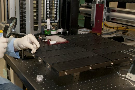 Gloved hands hold a magnifying lens and a glass slide beside a laboratory microarray instrument