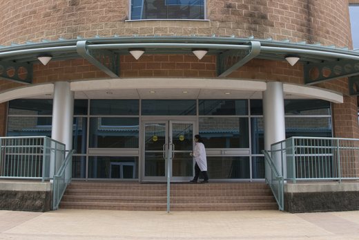 The curved glass entrance of an FDA research building, with a scientist in a lab coat walking toward the doors