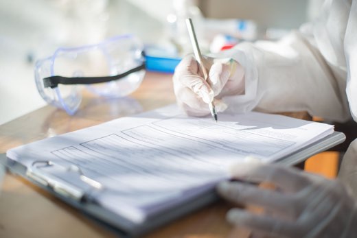 A gloved hand completing a multi-page laboratory record